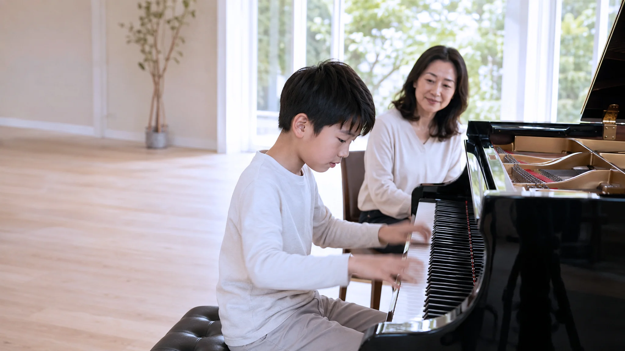 A boy playing a grand piano with his teacher beside him in a bright room